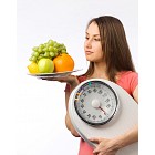 Young woman holding a weight scale and plate with fresh fruit 